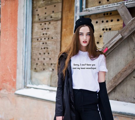 Fashionable long legs brunette model in long black cloak posed outdoor at winter day against old grunge wall with broken windows.